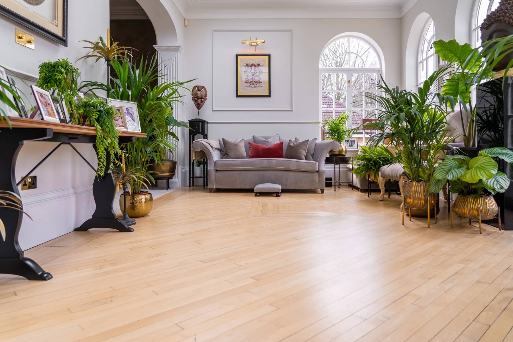 Polished timber flooring in a bright interior with arched windows, plants and a sofa